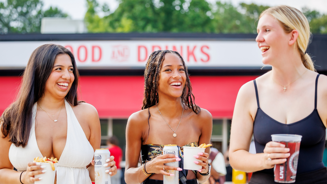 Three young women holding food and drinks.
